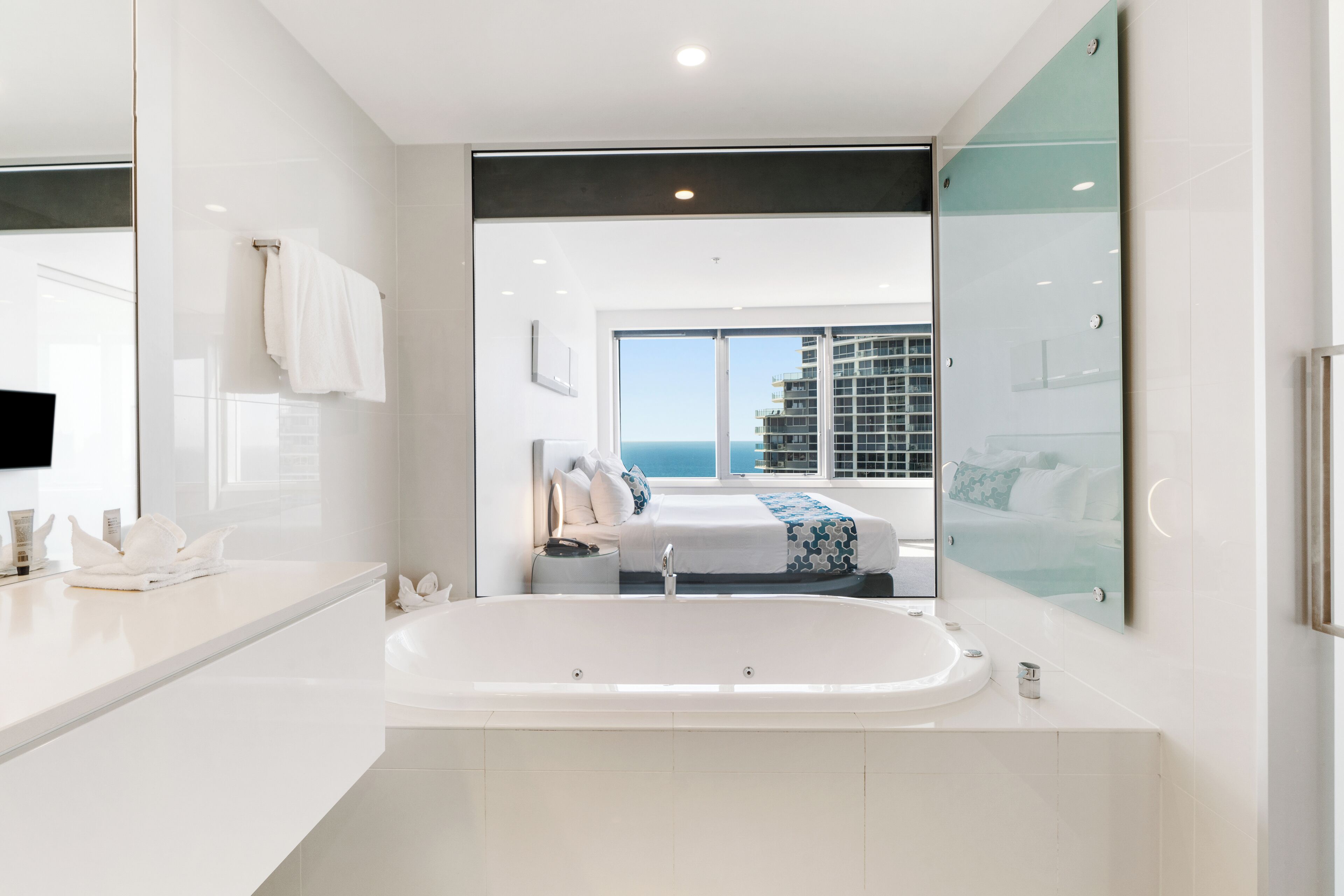 A modern bathroom with a large bathtub, a separate shower area, and a view of the sea through large windows.