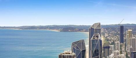 A coastal cityscape with modern skyscrapers, a beach, and a clear blue sky.