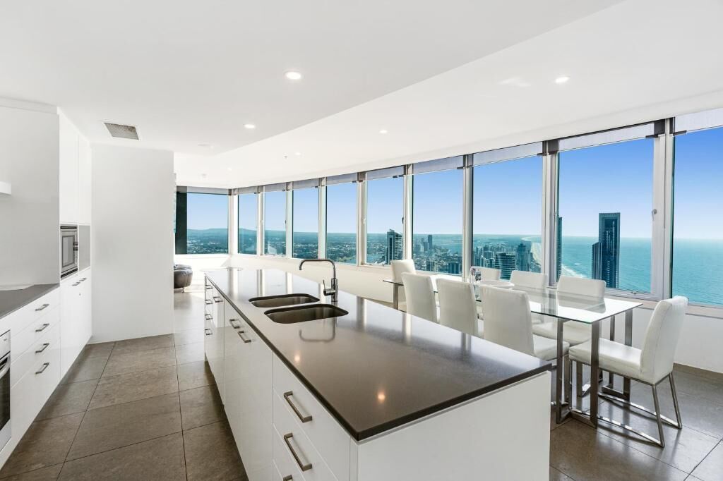 Una cocina moderna con una isla grande, armarios blancos y vistas a la ciudad y al océano.