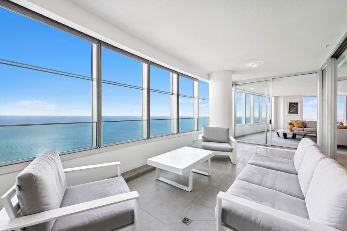 A modern interior with a large window overlooking the sea, a white sofa, a white coffee table, and a minimalist design.