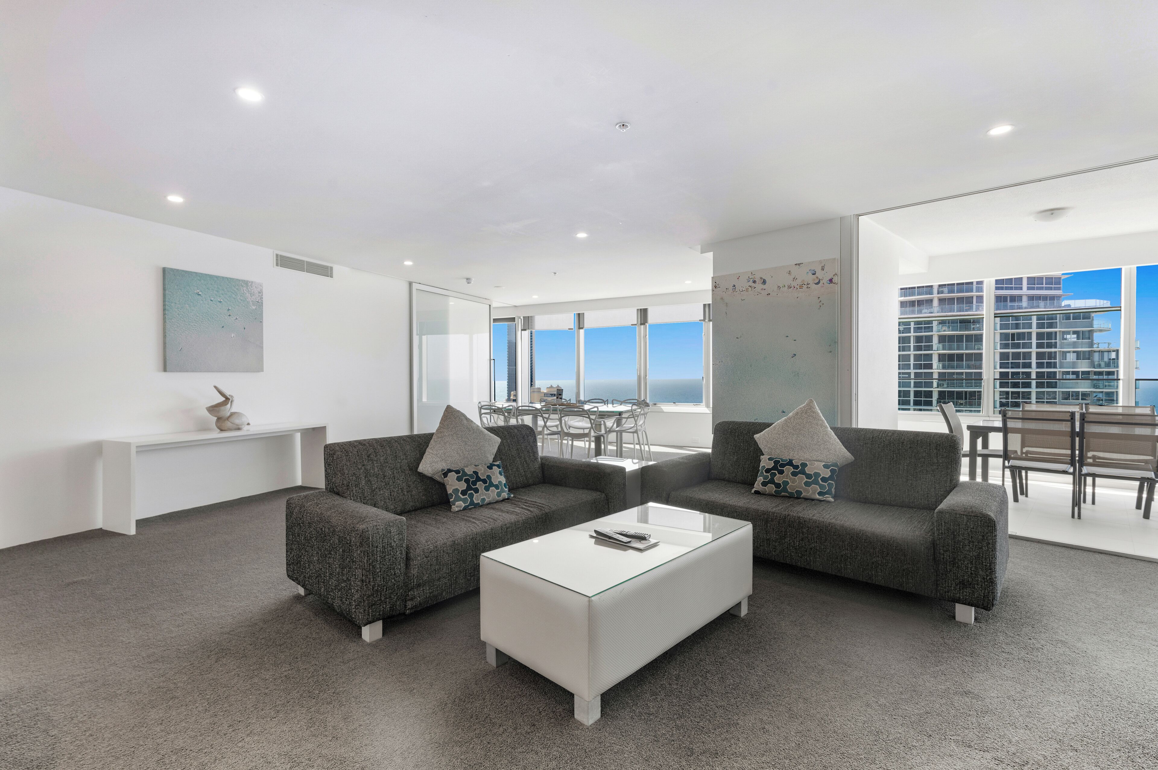 A modern living room with two grey sofas, a white coffee table, and a view of the sea through large windows.