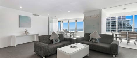 A modern living room with two grey sofas, a white coffee table, and a view of the sea through large windows.
