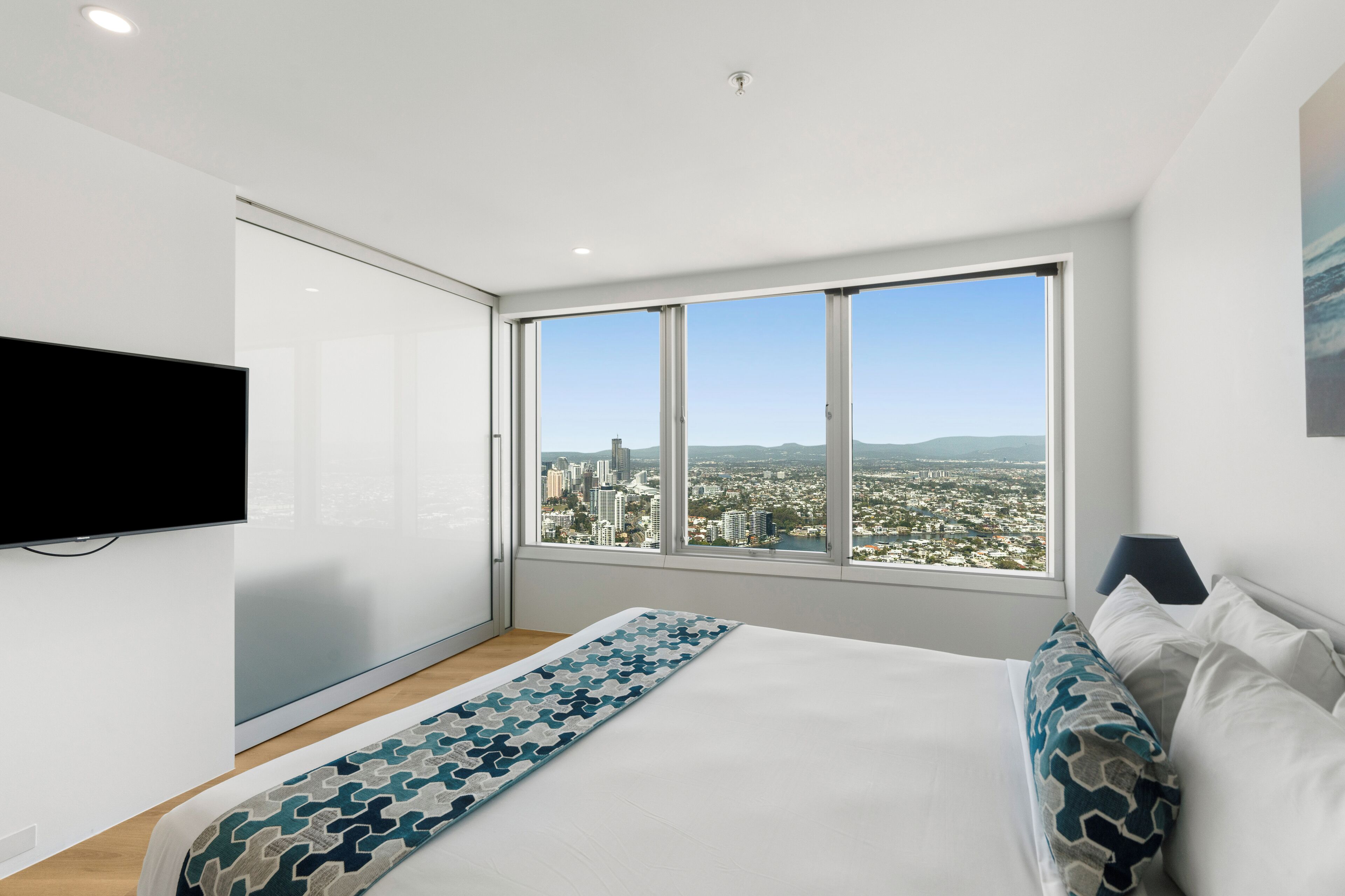 A modern bedroom with a large window, a bed, and a flat-screen TV.