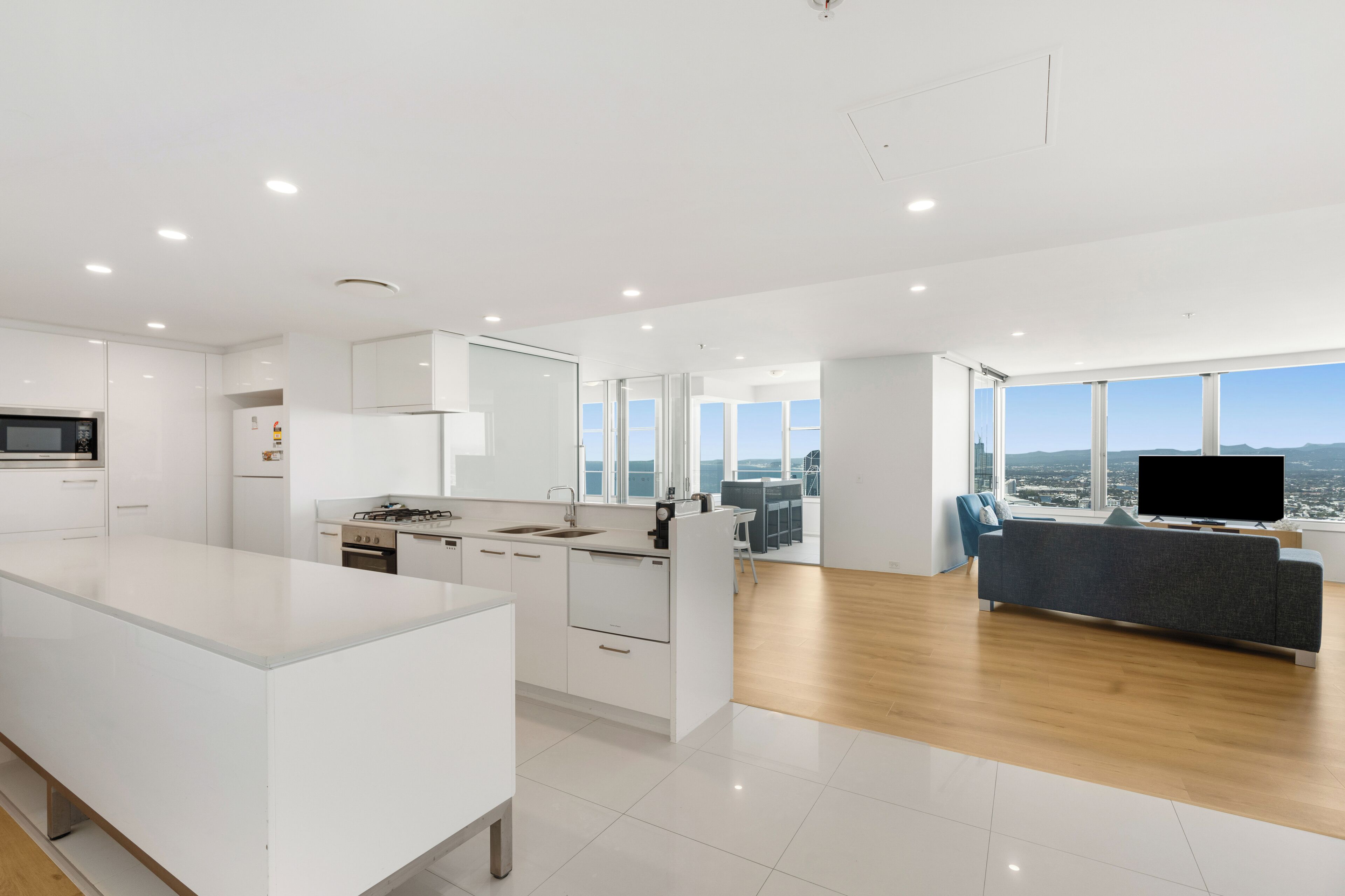 A modern kitchen with white cabinetry, a central island, and a large window overlooking a cityscape.