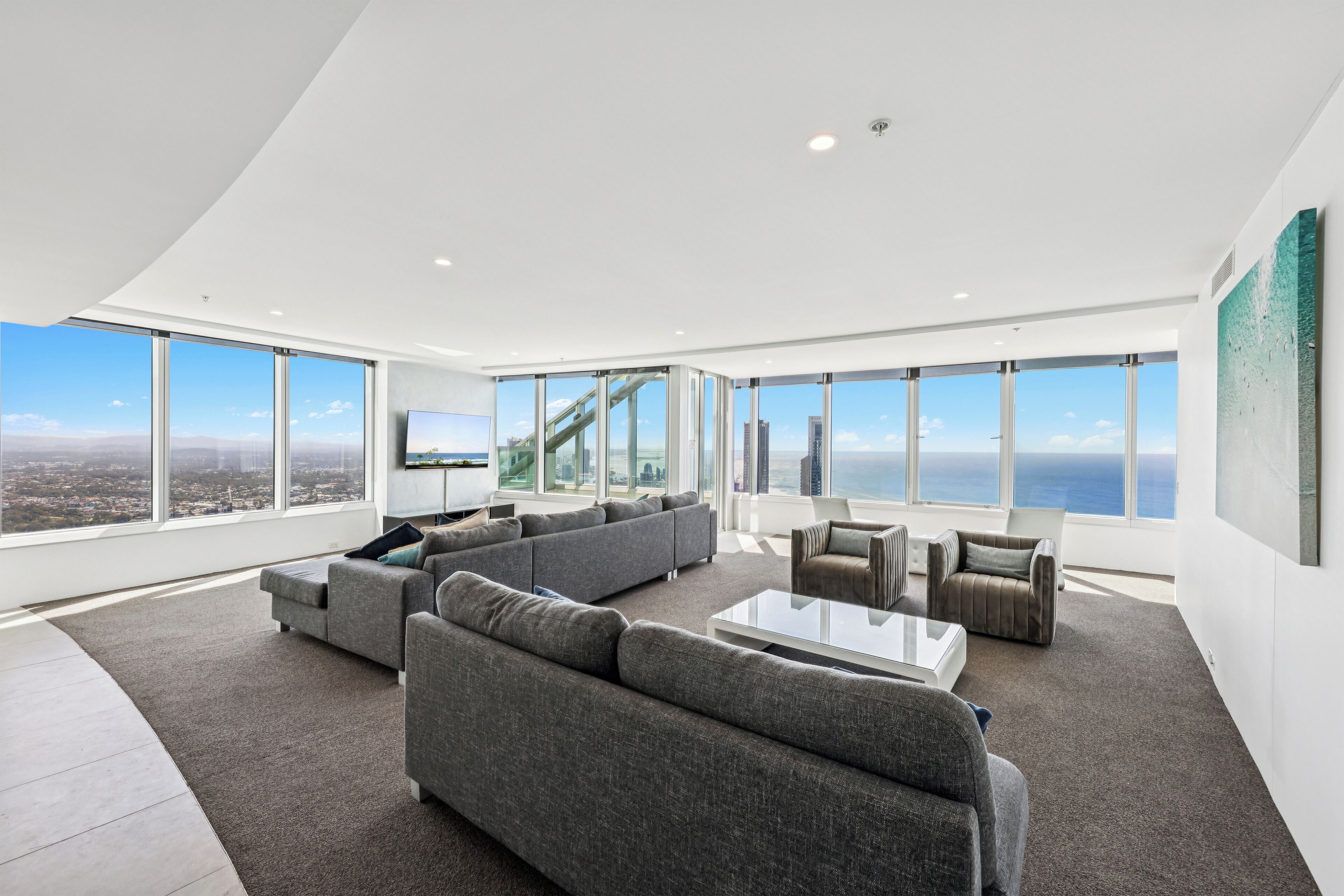 A modern living room with large windows, a sectional sofa, a coffee table, and a TV.