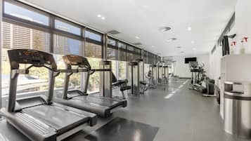 A modern gym with treadmills, weight machines, and a large window providing a view of buildings outside.