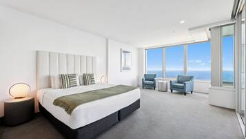 A modern hotel room with a large bed, two side tables, a seating area with chairs, and a large window offering a view.