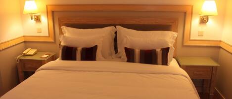 A hotel room with a large bed, two bedside lamps, a bedside telephone, and a small wooden nightstand.