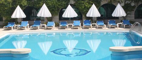 Een zwembad met blauw water, omringd door ligbedden en witte parasols.
