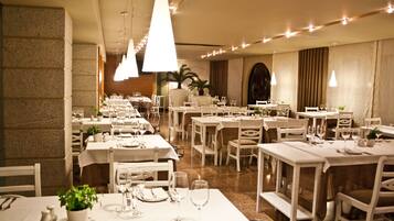 Restaurante com várias mesas preparadas para refeições, com toalhas de mesa brancas e cadeiras.