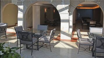 A spacious outdoor patio with modern furniture, stone arches, and a view into the interior dining area.