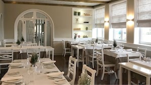 Un comedor con varias mesas dispuestas para el servicio, un arco central y estantes con adornos.