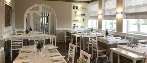 Un comedor con varias mesas dispuestas para el servicio, un arco central y estantes con adornos.
