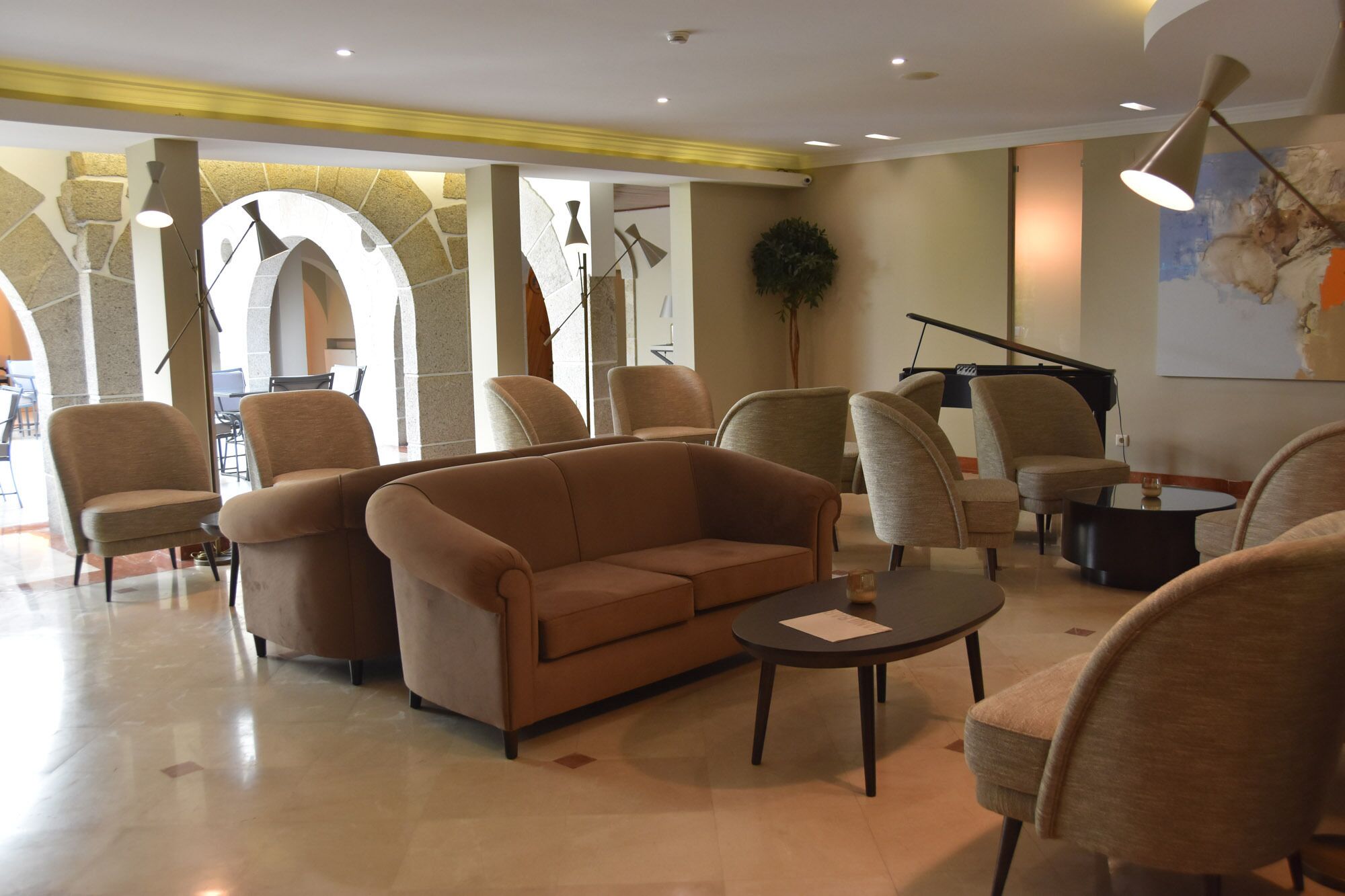 A spacious lobby with a sofa, armchairs, a piano, and a large plant.
