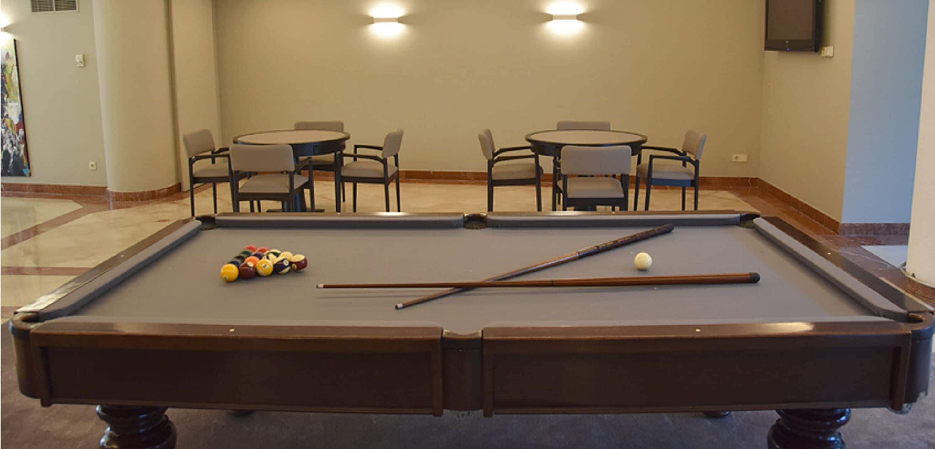 A pool table with balls and cues, surrounded by four chairs and two tables.