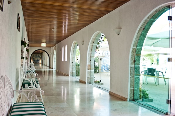 A corridor with arched windows, a wooden ceiling, and a row of green-striped chairs.
