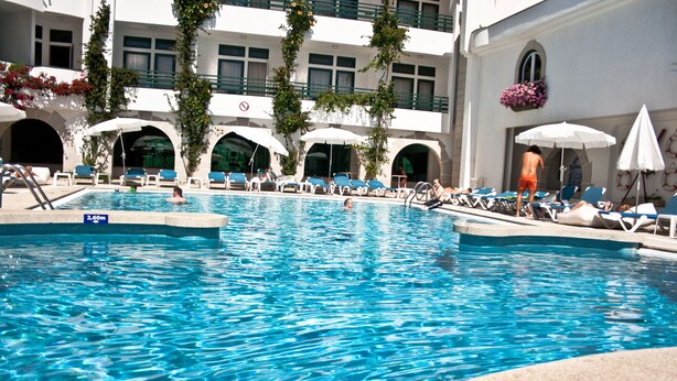Una piscina con agua cristalina azul, rodeada de sillas de descanso y sombrillas.