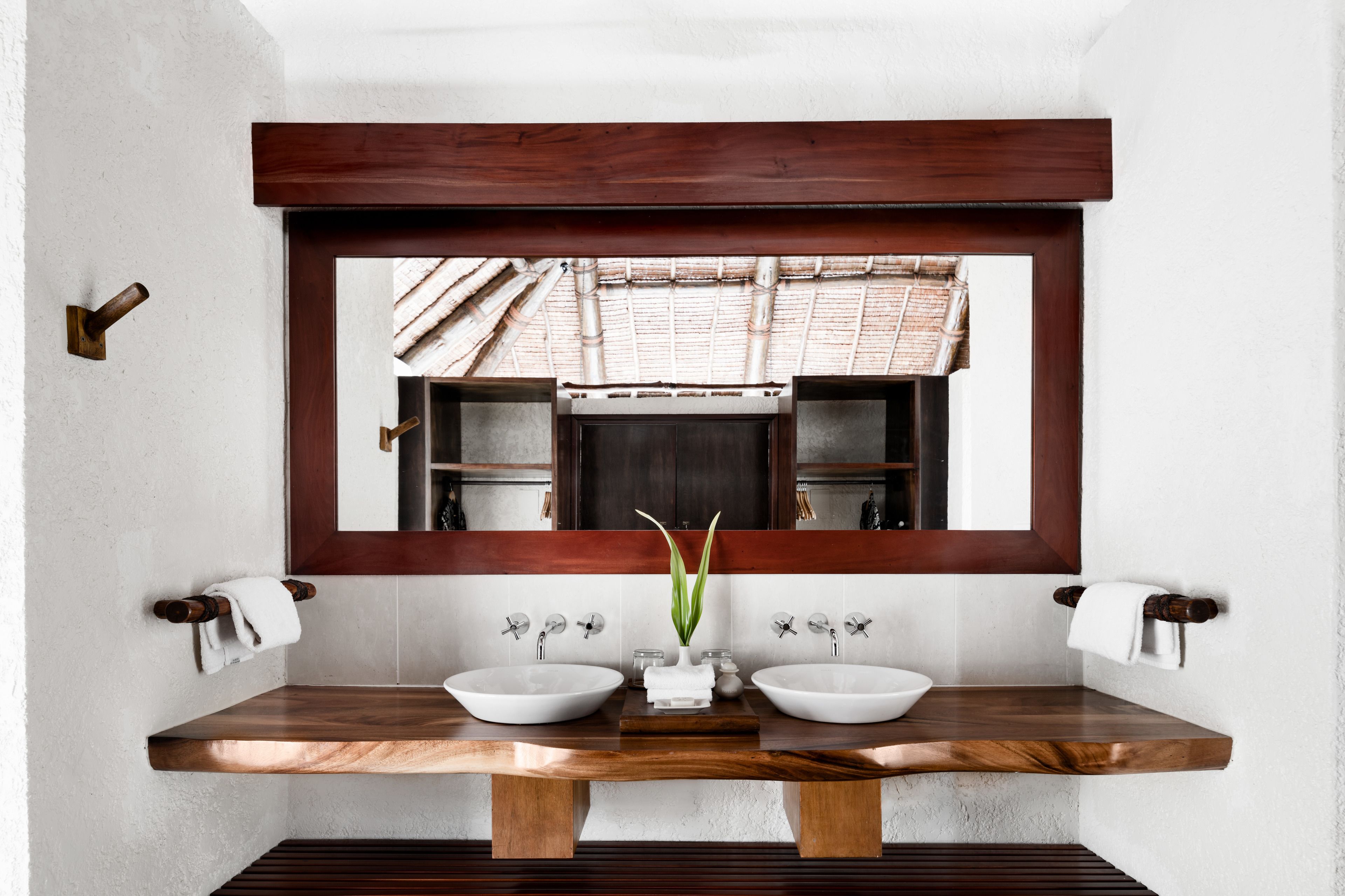 A bathroom with a wooden vanity, two sinks, a mirror, and a view of a traditional tiled roof through the mirror.