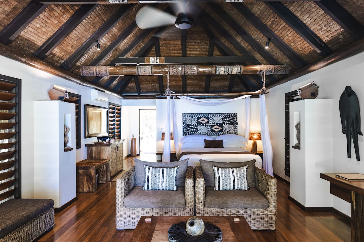 A spacious room with a high ceiling, a large bed, two wicker sofas, and a ceiling fan.