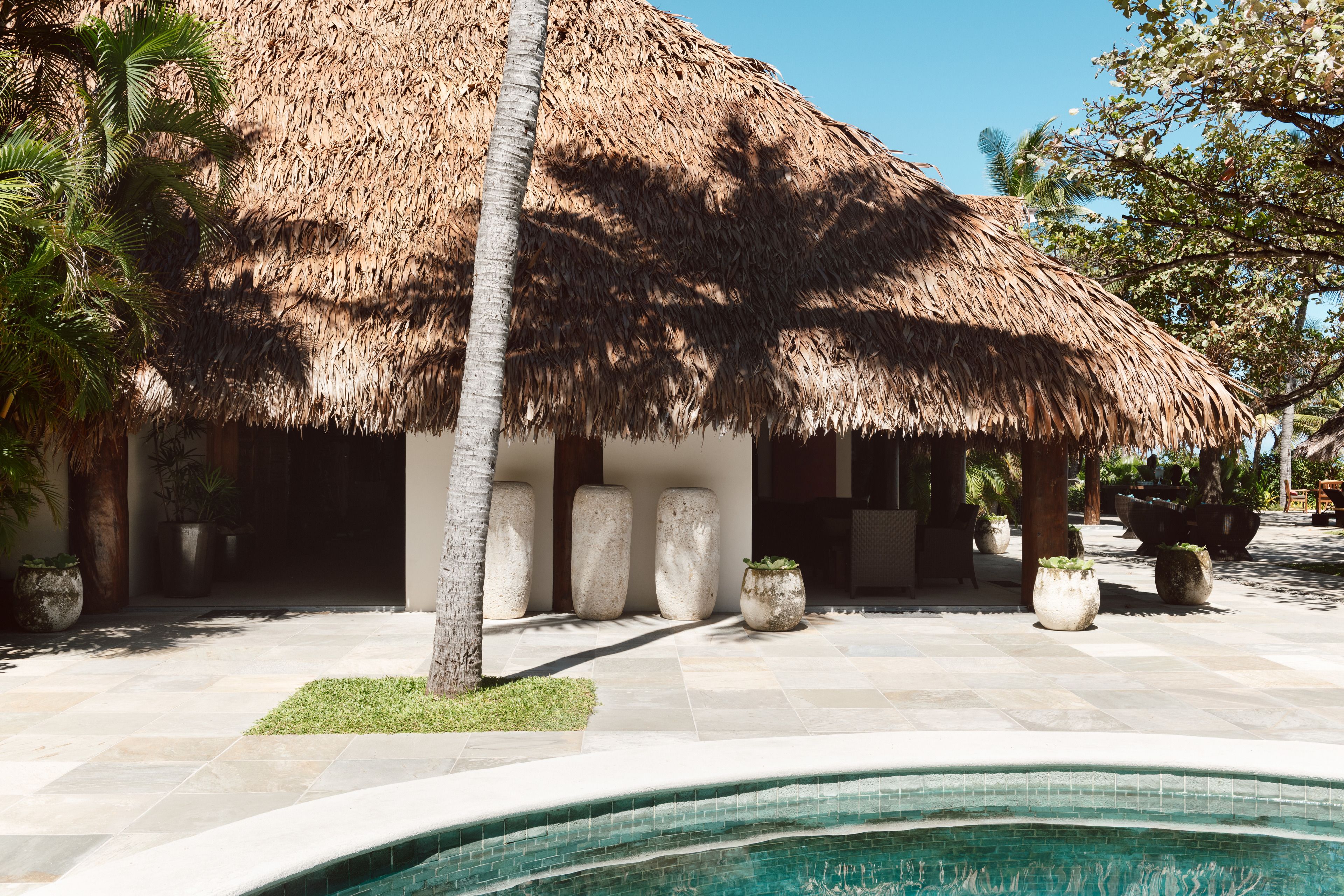 A pool area with a thatched-roof structure, stone pillars, and potted plants.