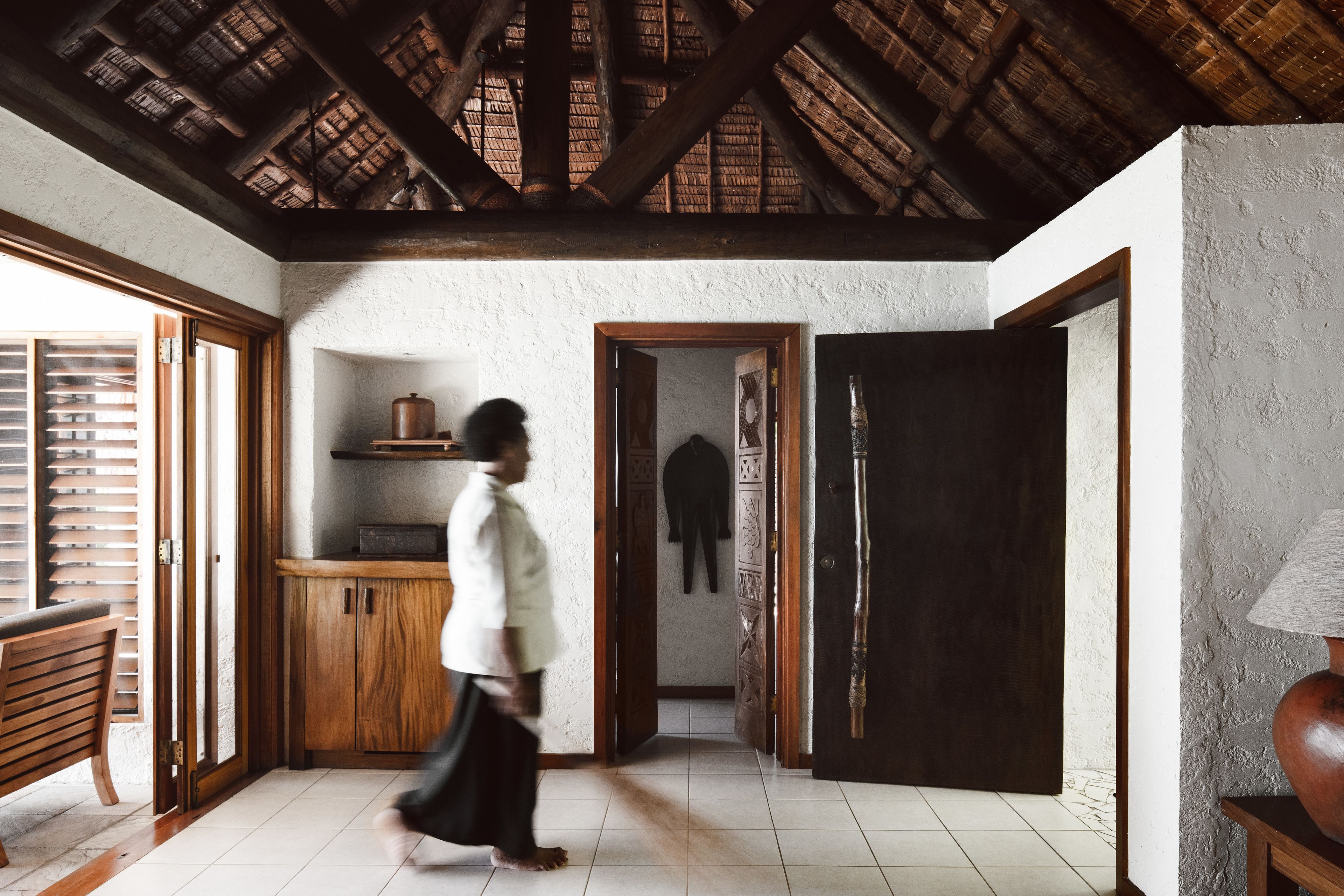 A room with a wooden ceiling, a bench, a wooden cabinet, and a door leading to another room.