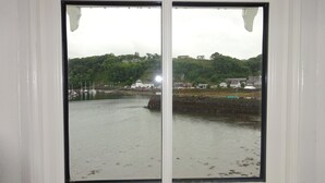 A window with a view of a harbor, buildings, and a hill with trees. - Tobermory Youth Hostel (Isle of Mull)