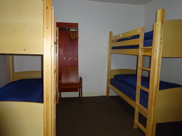 A room with two bunk beds, a wooden chair, and a red curtain. - Tobermory Youth Hostel (Isle of Mull)