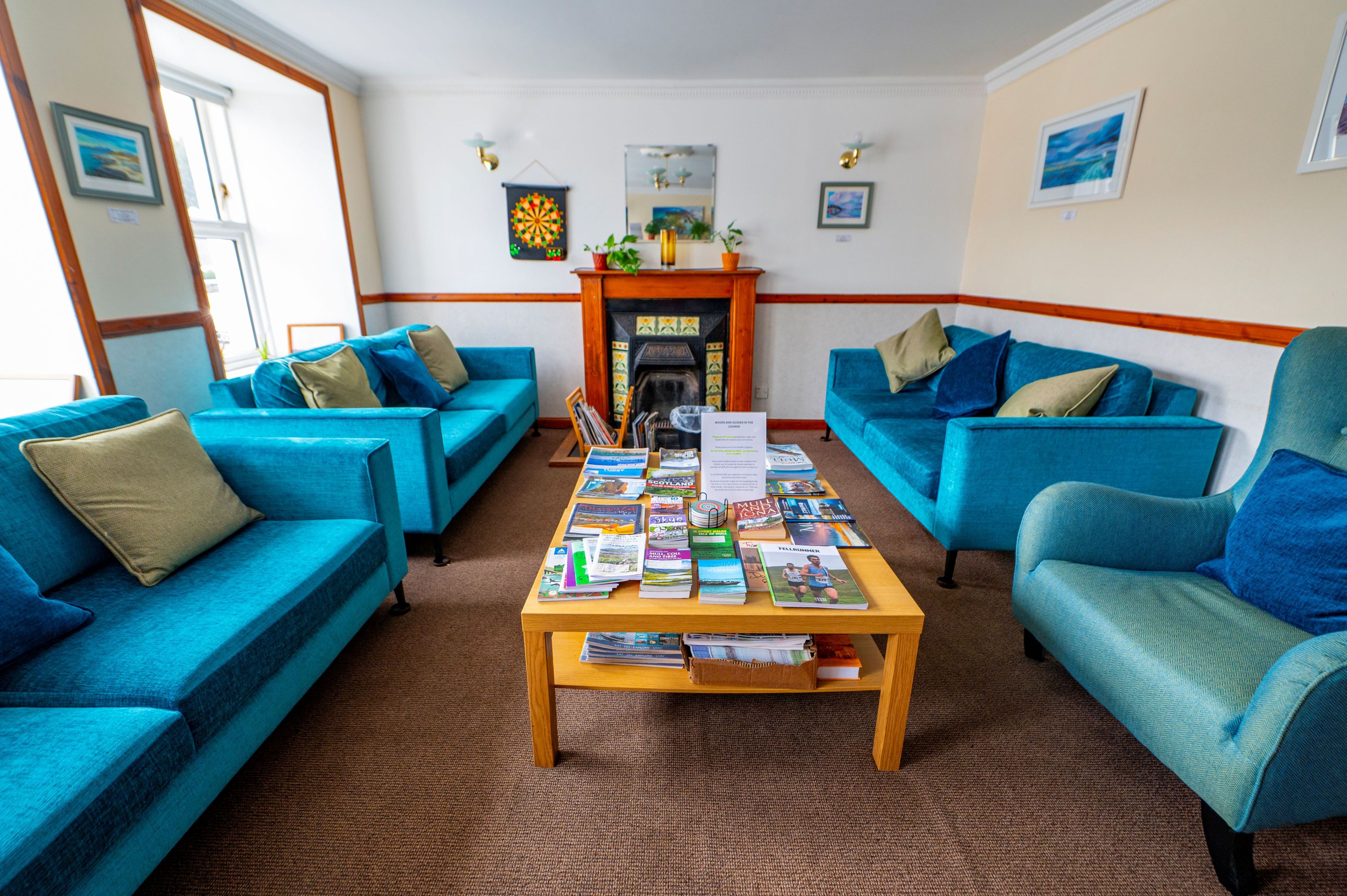 A room with two blue sofas, a wooden coffee table with magazines, a fireplace, and a dartboard on the wall.