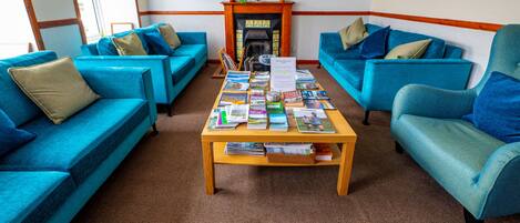 A room with two blue sofas, a wooden coffee table with magazines, a fireplace, and a dartboard on the wall.