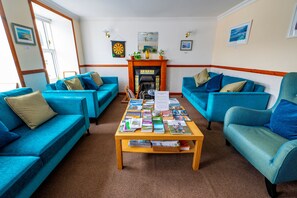 A room with two blue sofas, a wooden coffee table with magazines, a fireplace, and a dartboard on the wall. - Tobermory Youth Hostel (Isle of Mull)