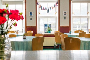 A dining area with round tables and chairs, a view of the outside through large windows, and a banner decoration. - Tobermory Youth Hostel (Isle of Mull)