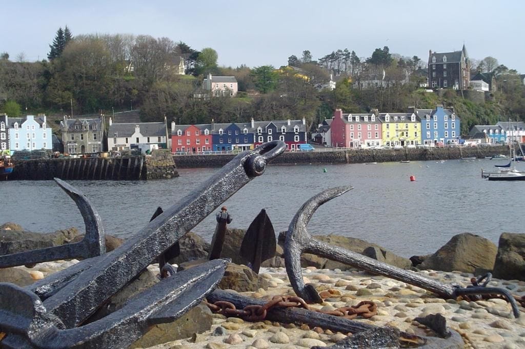 A coastal town with colorful buildings, a rocky shoreline, and a prominent anchor sculpture.