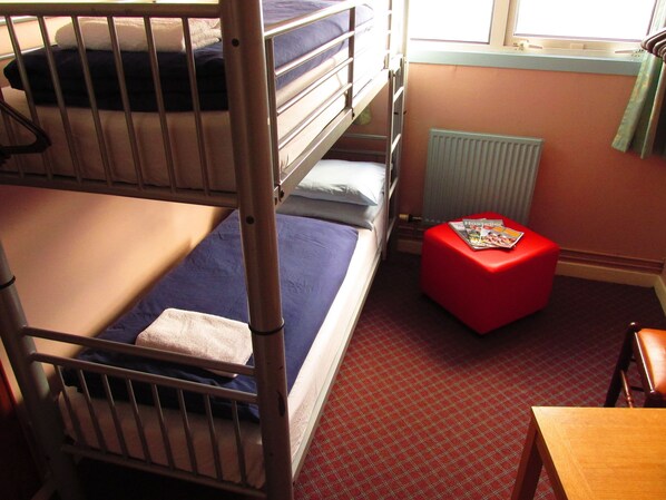 A bunk bed room with a red ottoman and a wooden table. - Broadford Youth Hostel (Strath)