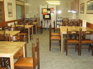 A dining area with wooden tables and chairs, a refrigerator, and a menu board. - Broadford Youth Hostel (Strath)