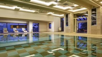 A spacious indoor swimming pool with a checkered floor, recessed lighting, and a view of the outdoors through large windows.