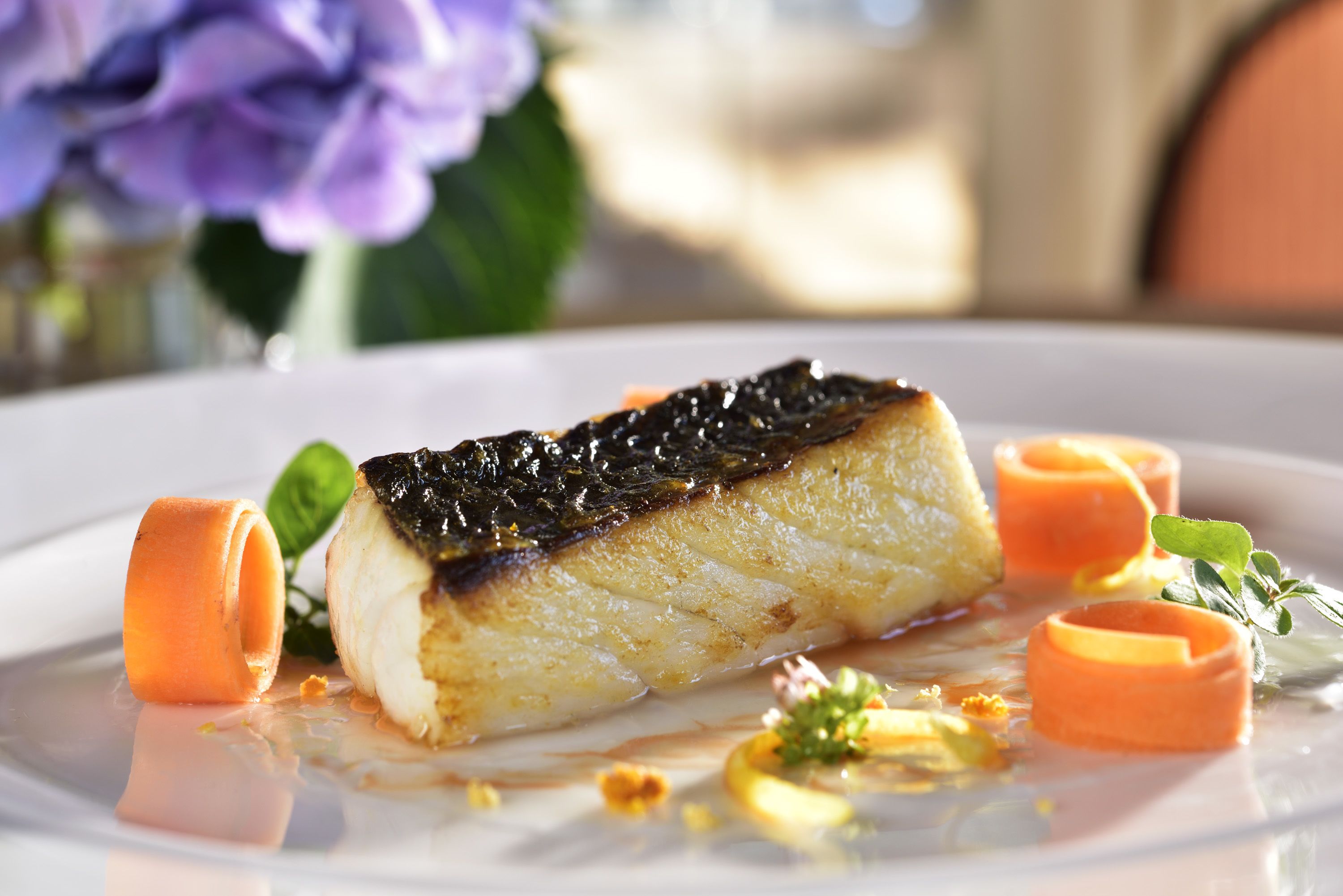 A plate with a piece of fish, carrot garnish, and a sauce.