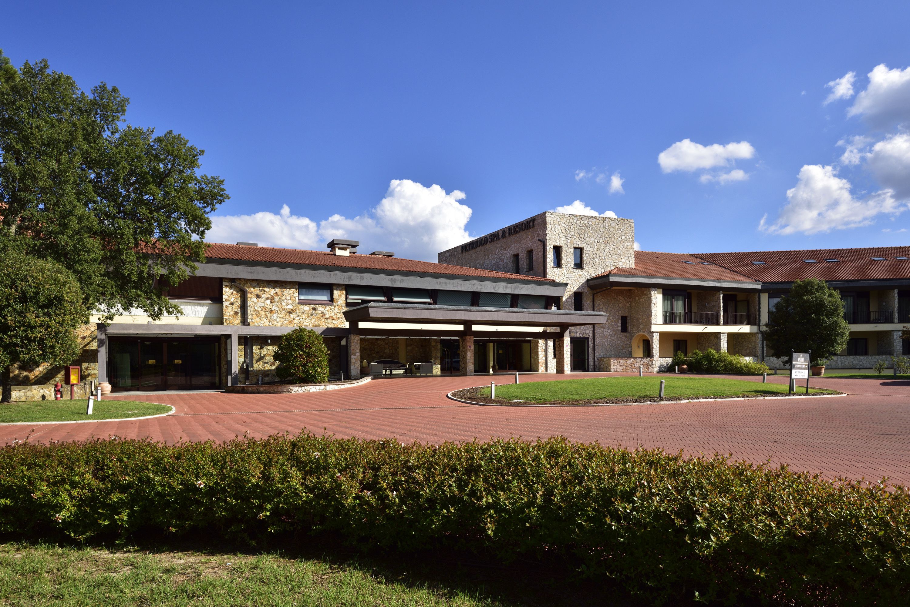 Un hotel con fachada de piedra, un vestíbulo cubierto y un patio ajardinado.