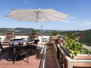 Un patio al aire libre con una mesa, sillas, una sombrilla grande y plantas en macetas.