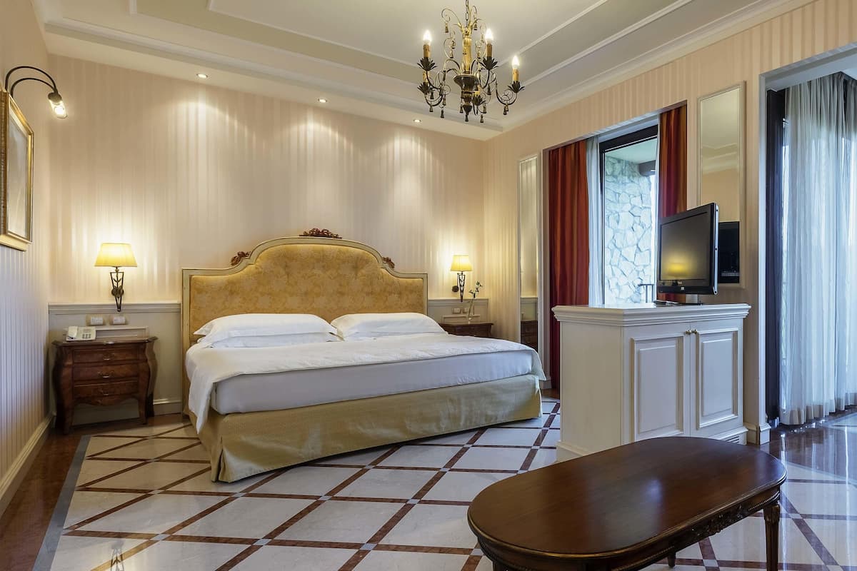 Una habitación de hotel con una cama grande, lámparas de noche, un televisor, un escritorio y una araña.