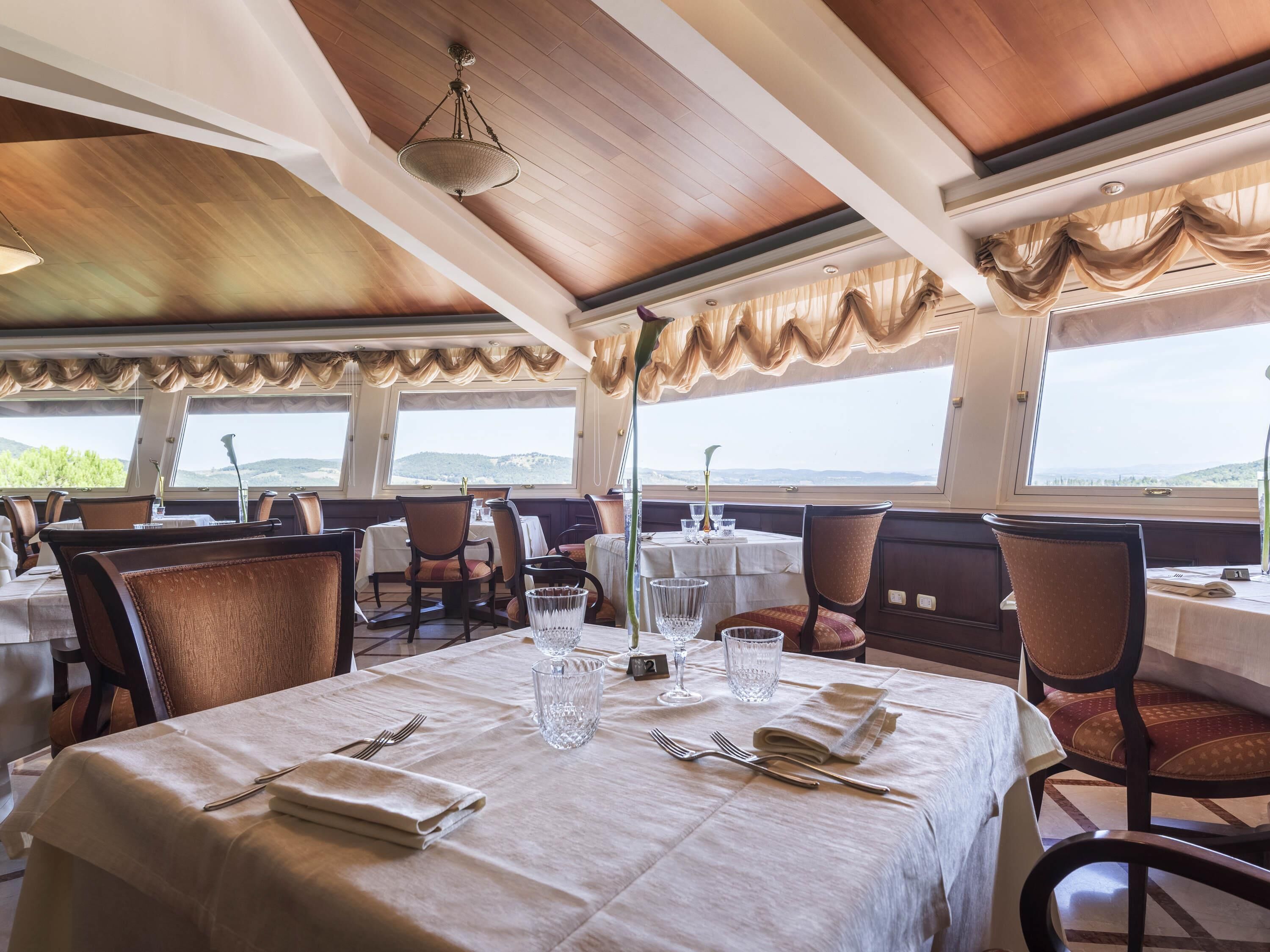 Un restaurante con mesas dispuestas para comer, ventanas amplias con vistas y un techo de madera.
