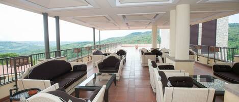 A covered outdoor seating area with wicker furniture and a view of the landscape.