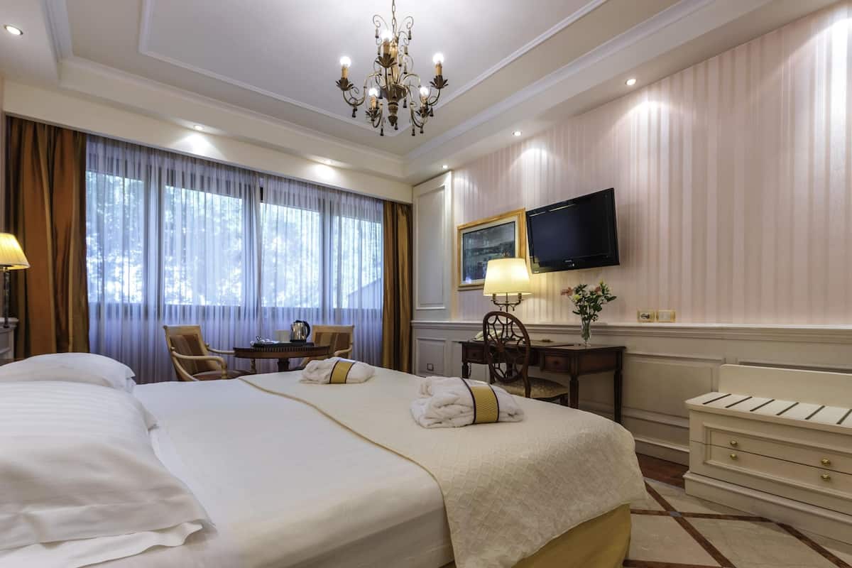 Ein Hotelzimmer mit einem großen Bett, einem Schreibtisch, einem Sessel, einem Fernseher und einer Kristallleuchter.