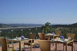 Una terraza con mobiliario de mimbre y una mesa lista para el desayuno, con vistas a un paisaje pintoresco.