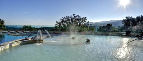 Una piscina con una fuente, sillas de descanso y vistas a montañas al fondo.