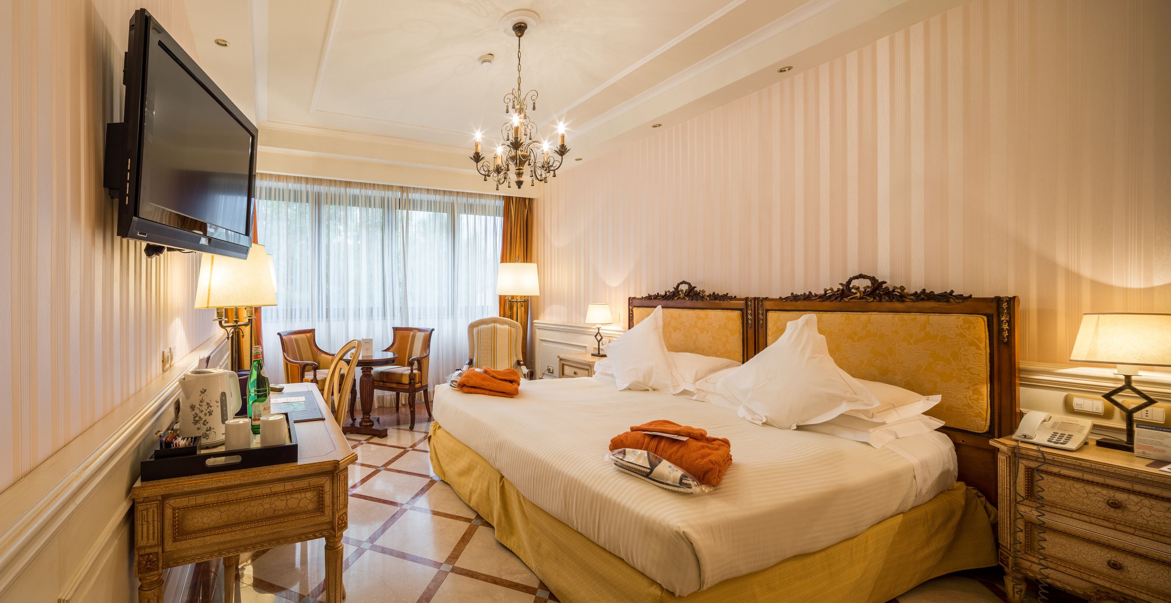 Ein Hotelzimmer mit Bett, Fernseher, Schreibtisch mit Lampe, Stuhl und Nachttisch mit Telefon.