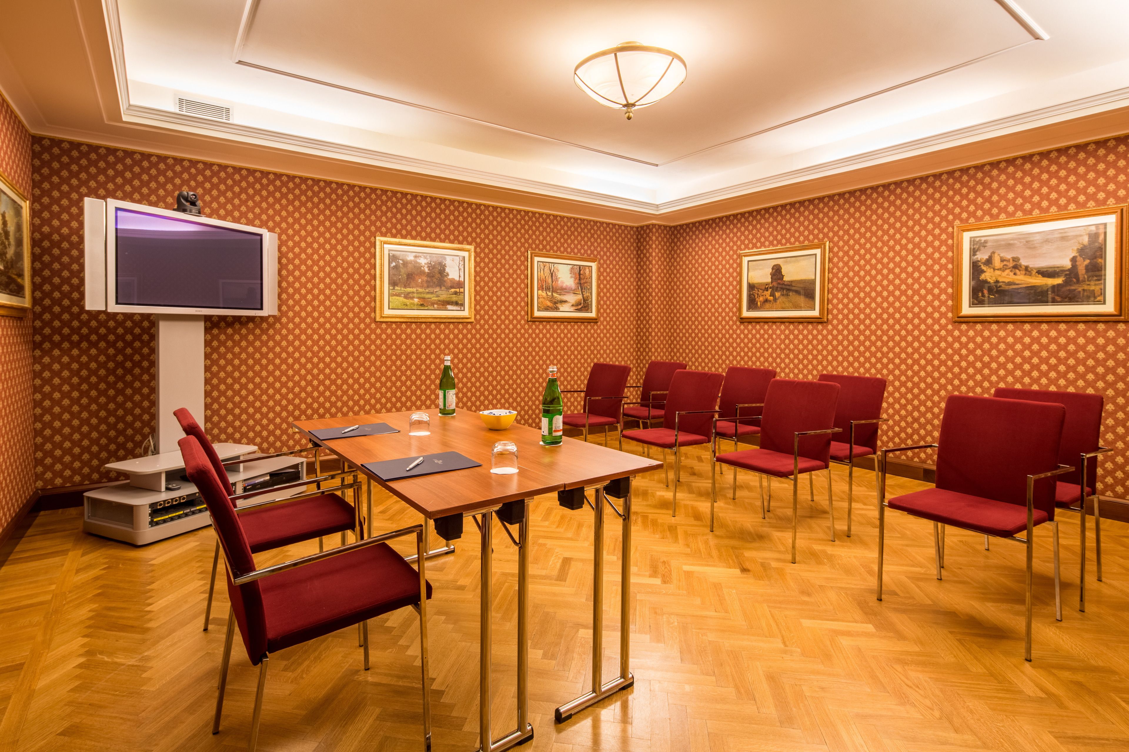 A conference room with a wooden table, red chairs, a flat-screen TV, and framed pictures on the walls.