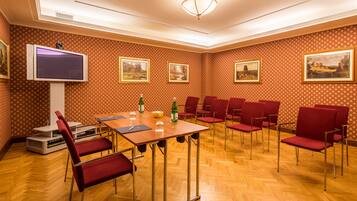 A conference room with a wooden table, red chairs, a flat-screen TV, and framed pictures on the walls.
