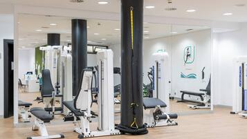Un gimnasio con diversas máquinas de ejercicio, un saco de boxeo grande y un muro con espejos.