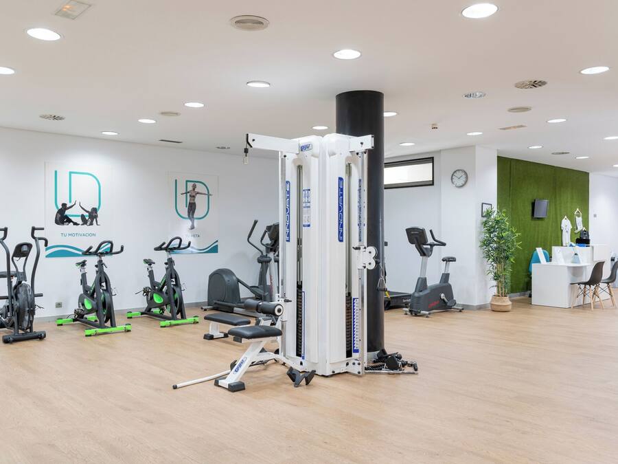 Un gimnasio moderno con diversos equipos de ejercicio, una recepción y una pared verde.