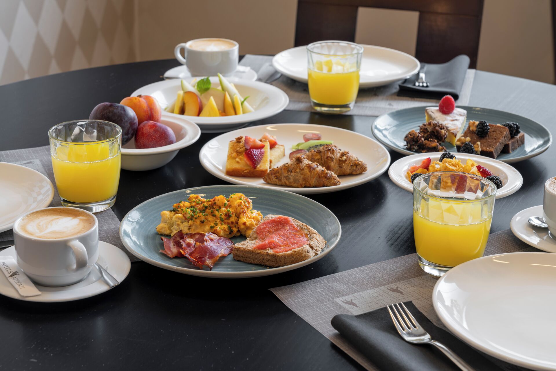 A breakfast setting with various dishes, including eggs, bacon, toast, and pastries, along with glasses of orange juice.